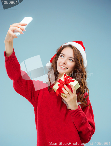Image of Girl dressed in santa hat with a Christmas gift and phone