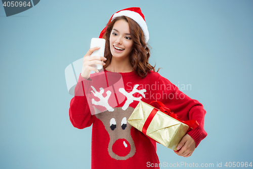 Image of Girl dressed in santa hat with a Christmas gift and phone
