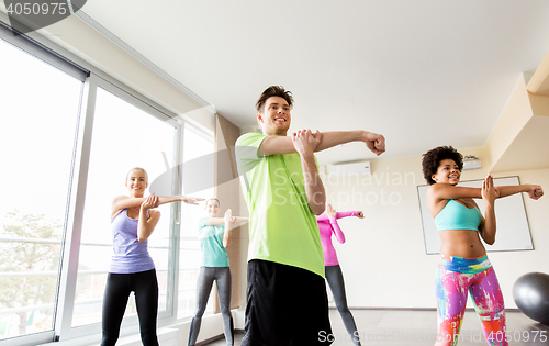 Image of group of smiling people stretching in gym