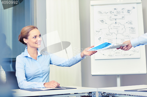 Image of businesswoman taking papers from someone in office