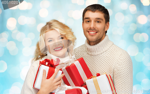 Image of happy couple in sweaters holding christmas gifts