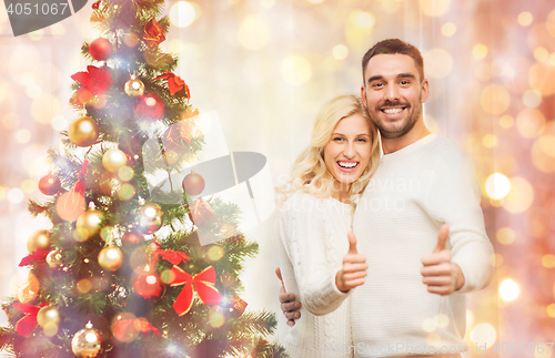 Image of happy couple showing thumbs up with christmas tree