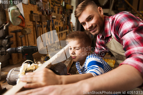 Image of father and little son with wood plank at workshop