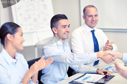 Image of smiling business team shaking hands in office