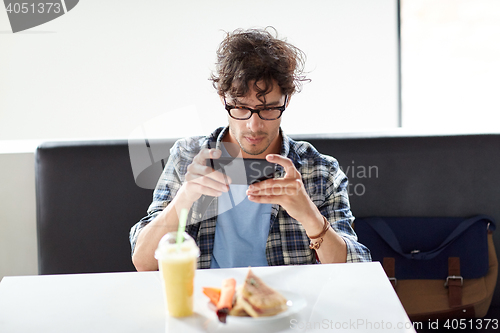 Image of man with smartphone photographing food at cafe
