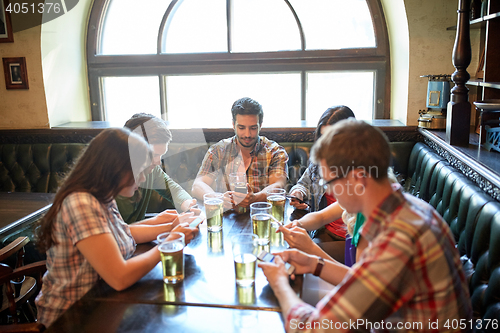 Image of friends with smartphones and beer at bar or pub