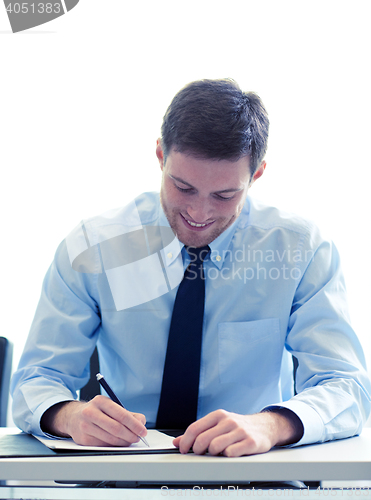 Image of smiling businessman signing papers in office