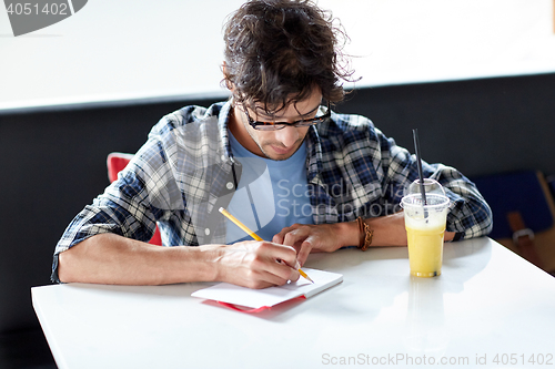 Image of man with notebook and juice writing at cafe