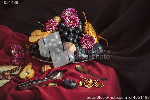 Image of The fruit bowl with grapes and plums against a maroon tablecloth