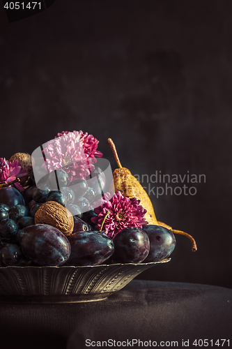 Image of The fruit bowl with grapes and plums against a dark wall
