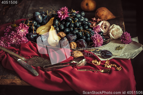 Image of The fruit bowl with grapes and plums against a maroon tablecloth