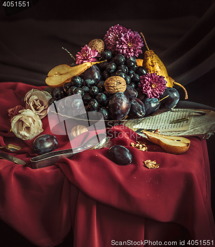 Image of The fruit bowl with grapes and plums against a maroon tablecloth