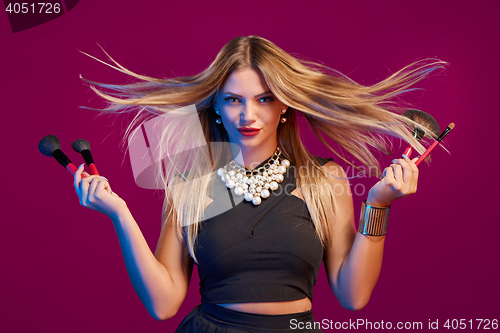 Image of Female stylist with hair flying holding makeup brushes