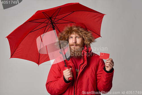 Image of Man in red winter jacket standing under umbrella and showing blank credit card