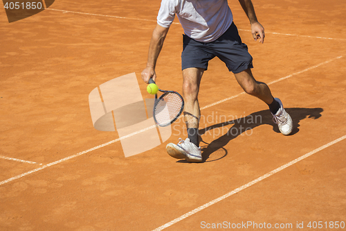 Image of Male tennis player in action on the clay court on a sunny day