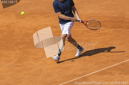 Image of Male tennis player in action on the clay court on a sunny day