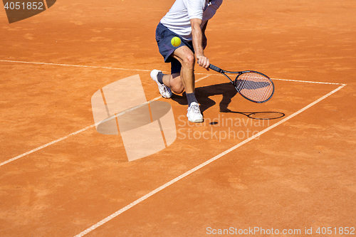 Image of Male tennis player in action on the clay court on a sunny day