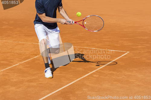 Image of Male tennis player in action on the clay court on a sunny day