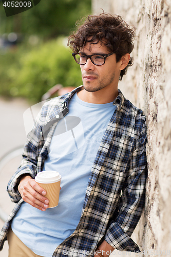 Image of man in eyeglasses drinking coffee over street wall