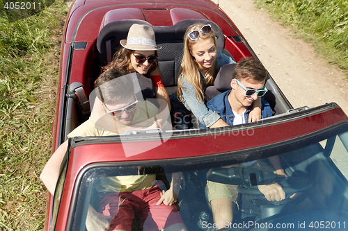 Image of happy friends driving in cabriolet car at country