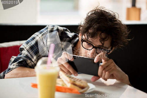 Image of man with smartphone photographing food at cafe