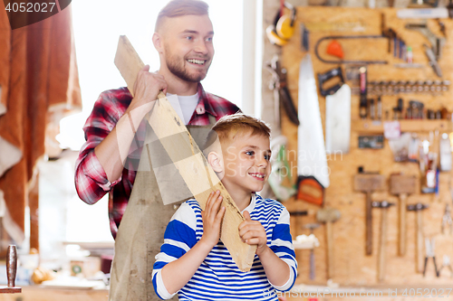 Image of happy father and son with wood plank at workshop