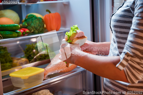 Image of Hungry Woman holding a sandwich in his hands and standing next t