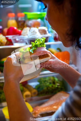 Image of Hungry Woman holding a sandwich in his hands and standing next t