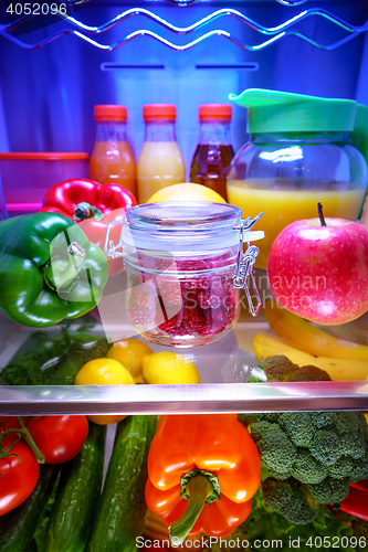 Image of Fresh raspberries in a glass jar on a shelf open refrigerator