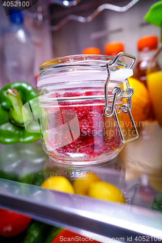 Image of Fresh raspberries in a glass jar on a shelf open refrigerator