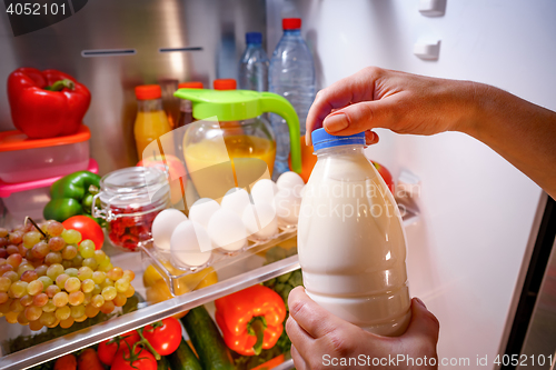 Image of Woman takes the milk from the open refrigerator