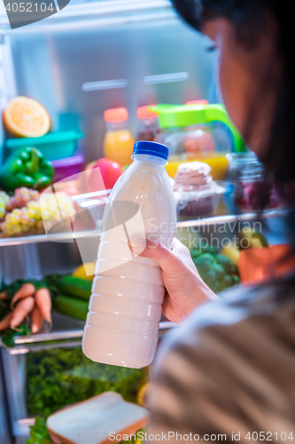 Image of Woman takes the milk from the open refrigerator