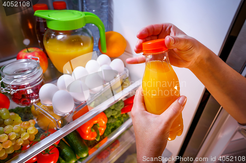 Image of Woman takes the Orange juice from the open refrigerator