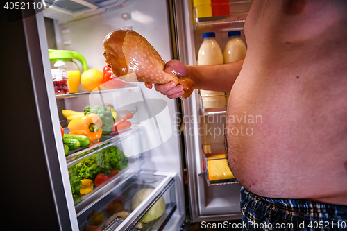 Image of Hungry man holding a turkey leg in his hands and standing next t