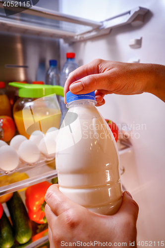 Image of Woman takes the milk from the open refrigerator