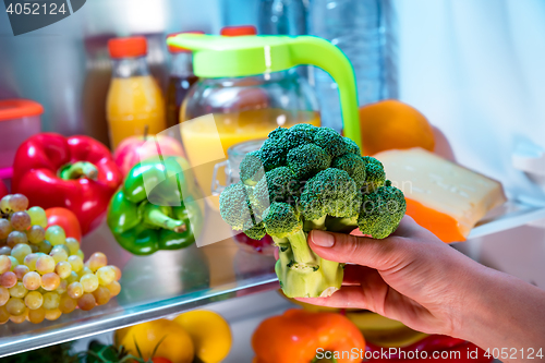 Image of Woman takes the broccoli from the open refrigerator.