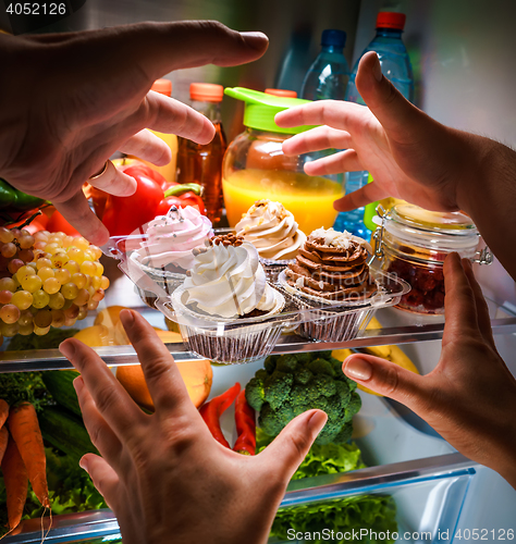 Image of Human hands reaching for sweet cake at night in the open refrige