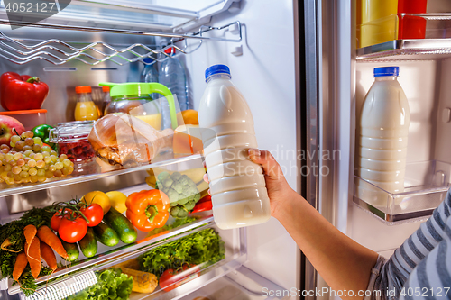 Image of Woman takes the milk from the open refrigerator