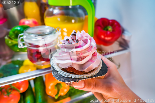 Image of Woman takes the sweet cake from the open refrigerator