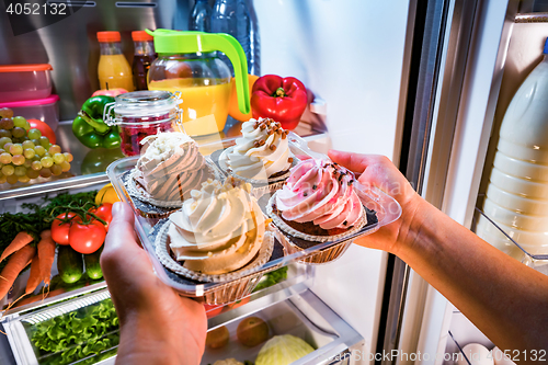 Image of Woman takes the sweet cake from the open refrigerator