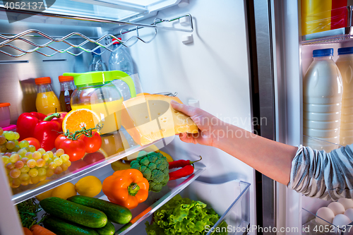 Image of Woman takes the piece of cheese from the open refrigerator