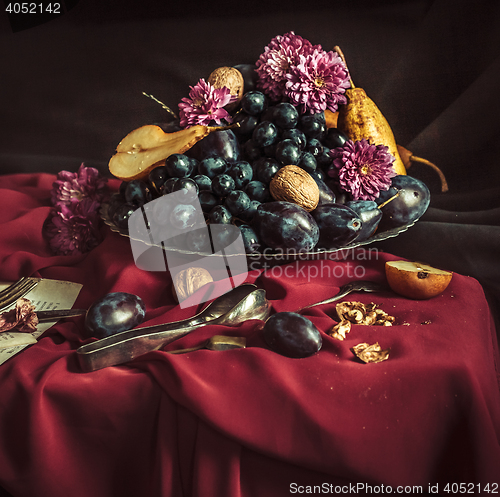 Image of The fruit bowl with grapes and plums against a maroon tablecloth