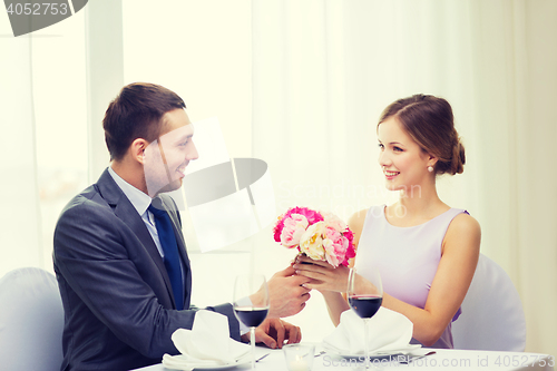 Image of smiling man giving flower bouquet at restaurant