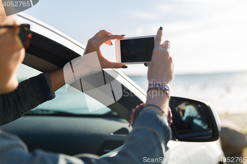 Image of happy young woman in car with smartphone at sea