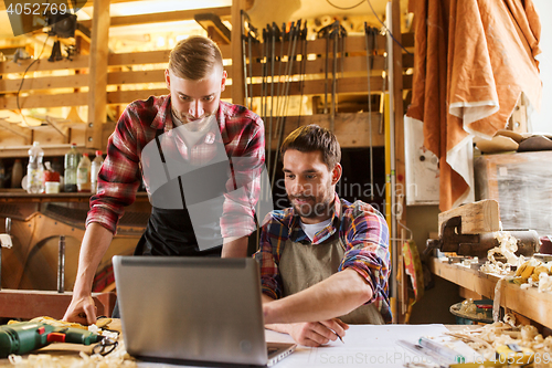 Image of carpenters with laptop and blueprint at workshop