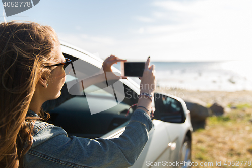 Image of happy young woman in car with smartphone at sea