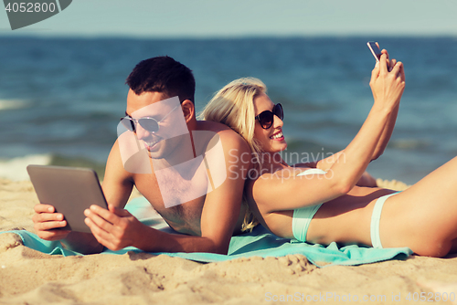 Image of happy couple with modern gadgets lying on beach