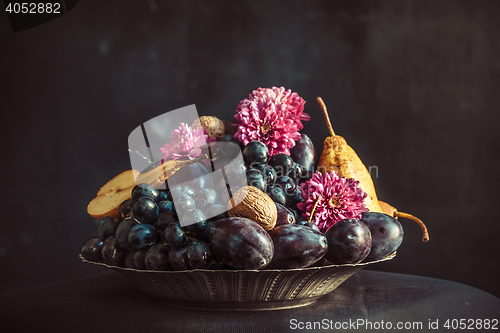 Image of The fruit bowl with grapes and plums against a dark wall