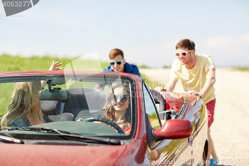 Image of happy friends pushing broken cabriolet car