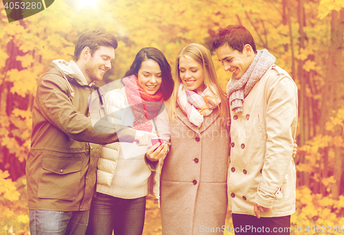 Image of smiling friends with smartphones in city park